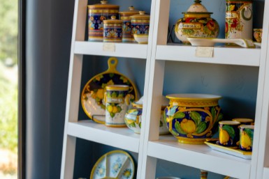 Ceramic canisters, bowls, cups and plates with hand painted lemons in a field of blue sitting on a white ladder display unit