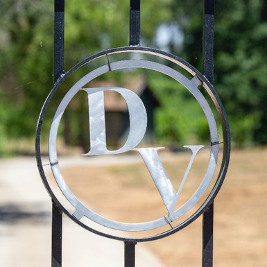 Metalwork letters D and V decorate a fence while greenery recedes into the distance down a dirt road